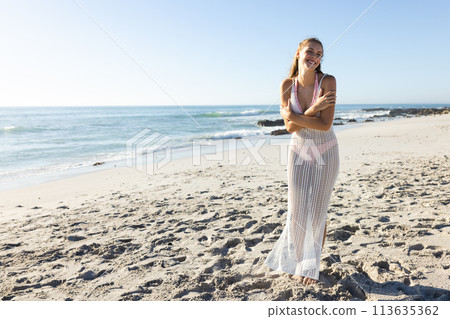 Young Caucasian woman stands on a sunny beach, with copy space 113635362