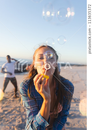 Young Caucasian woman blows bubbles on a sunny beach 113635372