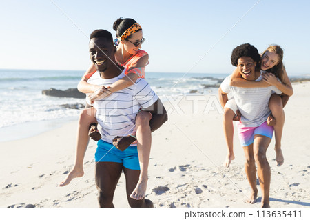 Diverse friends enjoy piggyback rides on a sunny beach 113635411