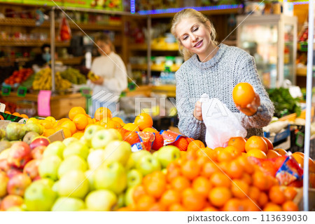 Positive female shopper looking for sweet oranges in supermarket 113639030