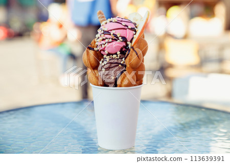 Belgian waffle with ice cream in paper cup on glass table of sidewalk cafe. fast food, take away summer sweet food Belgian waffle with ice cream in paper cup on glass table of sidewalk cafe. fast food, take away summer sweet food 113639391
