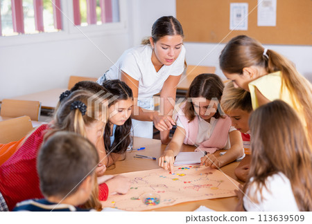 Children and teacher playing together educational board game in class Children and teacher playing together educational board game in class 113639509