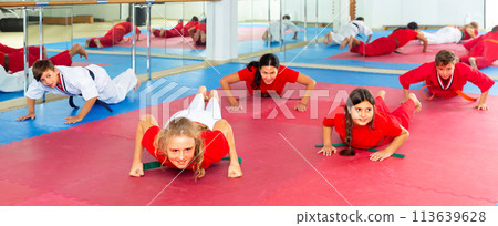 Group of teenagers together with female trainer doing warm-up and push-ups in gym 113639628