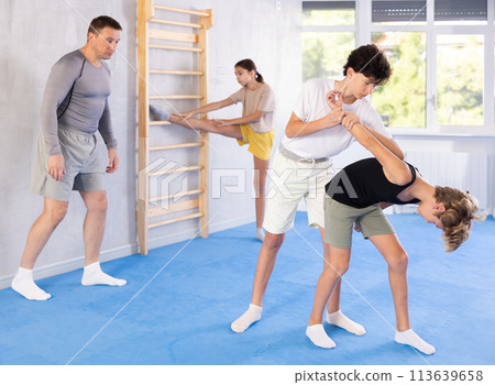 Two preteen boys learn to do power grabs in pairs during a self-defense lesson under the guidance of trainer in the gym 113639658