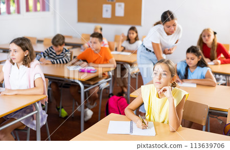 Interested diligent preteen schoolgirl writing exercises at lessons 113639706