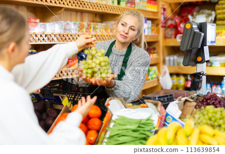Female grocery store worker handing grape to customer after payment at checkout closeup Female grocery store worker handing grape to customer after payment at checkout closeup 113639854