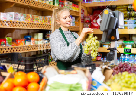 Focused saleswoman weighing grape on scale in grocery store 113639917