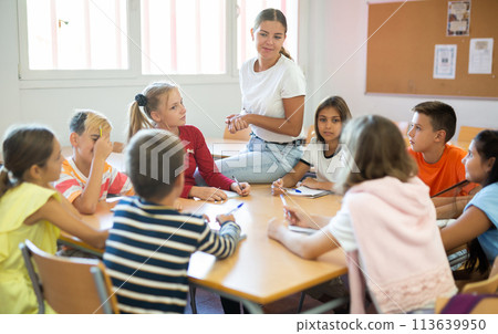 Female teacher giving lesson for preteen schoolchildren sitting around common desk Female teacher giving lesson for preteen schoolchildren sitting around common desk 113639950