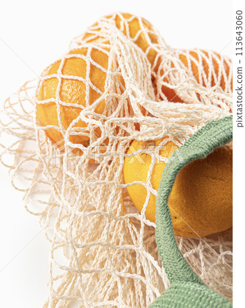 Fresh unpeeled oranges placed in reusable white mesh bag 113643060