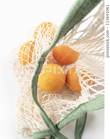 Fresh unpeeled oranges placed in reusable white mesh bag 113643061