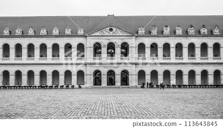 Visitors walk across the cobblestone courtyard of Les Invalides under an overcast Paris sky, France. Black and white image. Visitors walk across the cobblestone courtyard of Les Invalides under an overcast Paris sky, France. Black and white image. 113643845