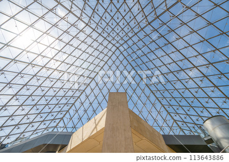 The geometric glass panels of the Louvre Pyramid, viewed from beneath against a clear blue sky in Paris, with interior structures visible. France 113643886