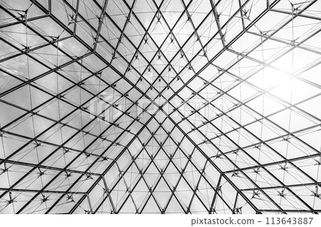 Underneath the Louvre Pyramid, the intricate glasswork contrasts against a blue sky on a clear day in Paris, France. Black and white image. 113643887