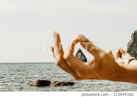 Yoga on the beach. A happy woman meditating in a yoga pose on the beach, surrounded by the ocean and rock mountains, promoting a healthy lifestyle outdoors in nature, and inspiring fitness concept. 113644192