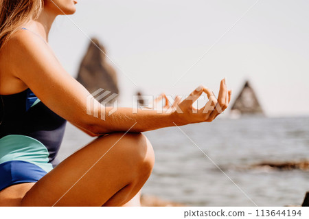 Yoga on the beach. A happy woman meditating in a yoga pose on the beach, surrounded by the ocean and rock mountains, promoting a healthy lifestyle outdoors in nature, and inspiring fitness concept. 113644194
