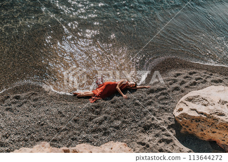 Woman red dress sea. Female dancer in a long red dress posing on a beach with rocks on sunny day 113644272