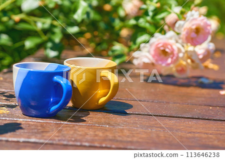 Tea time. Coffee break. Blue yellow cups on wooden in blooming garden Tea time. Coffee break. Blue yellow cups on wooden in blooming garden 113646238