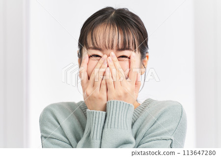 A woman covers her face with her hands in delight at a surprise 113647280