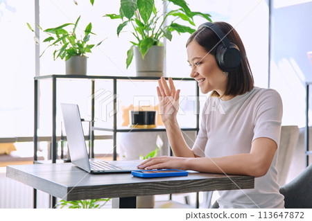 Young woman in headphones having work video chat conference call, using laptop in cafe Young woman in headphones having work video chat conference call, using laptop in cafe 113647872