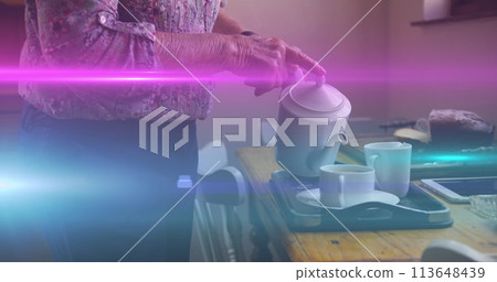 Image of coloured lights moving over senior woman pouring tea at home 113648439