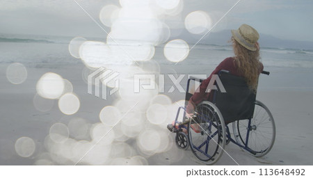 Image of light spots over disabled cuacasian woman sitting in wheelchair at beach 113648492