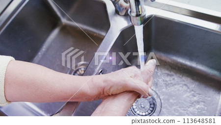 Image of light moving over hands of senior woman washing hands in kitchen sink 113648581