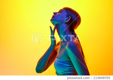 Side view photo of young sensual woman touching her neck in neon light against yellow gradient studio background. Side view photo of young sensual woman touching her neck in neon light against yellow gradient studio background. 113649705