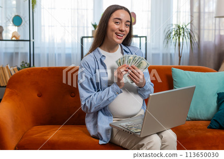 Happy pregnant woman counting money pressing keyboard keys on laptop buying online shopping at home Happy pregnant woman counting money pressing keyboard keys on laptop buying online shopping at home 113650030