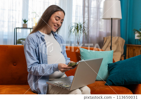 Happy pregnant woman counting money pressing keyboard keys on laptop buying online shopping at home 113650031