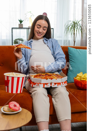 Pregnant woman eating unhealthy junk fatty fast food pizza popcorn crisp watching movie at home 113650085
