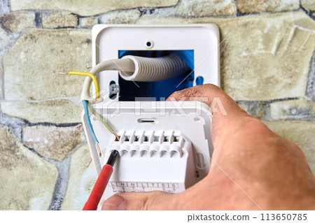 Wiring new electrical socket of thermostat in stone wall, Electrician Installing, connecting live neutral and ground wires, work involved in electrical fittings. Wiring new electrical socket of thermostat in stone wall, Electrician Installing, connecting live neutral and ground wires, work involved in electrical fittings. 113650785