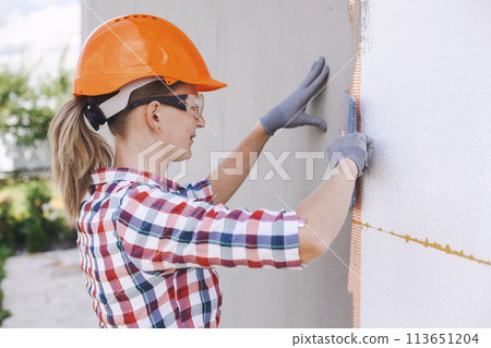 Insulation of the house with polyfoam. The worker is checking with the construction level the accuracy of the installation of polystyrene board on the facade. 113651204