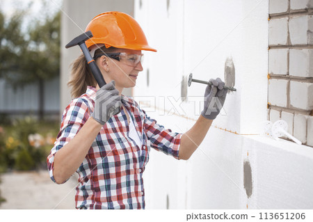 Insulation of the house with polyfoam. The worker is checking with the construction level the accuracy of the installation of polystyrene board on the facade. 113651206