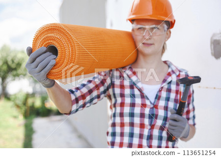 The woman with rolls of reinforcing fiberglass. Insulation of the house with polyfoam board on the facade 113651254