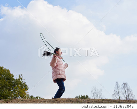 一個小女孩在冬季公園裡高興地玩跳繩 一個小女孩在冬季公園裡高興地玩跳繩 113652042