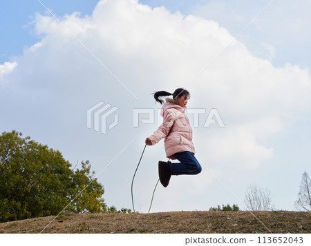 A young elementary school girl playing with a skipping rope in a winter park A young elementary school girl playing with a skipping rope in a winter park 113652043