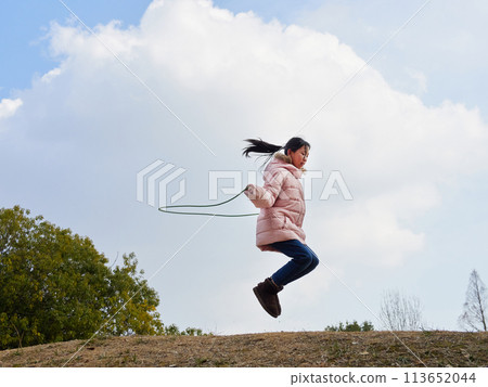A young elementary school girl playing with a skipping rope in a winter park 113652044