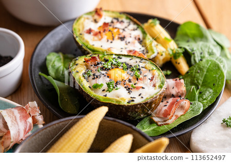 Cooking Avocado with Egg and Bacon. The girl prepares a healthy meal, close-up of her hands and Cooking Avocado with Egg and Bacon. The girl prepares a healthy meal, close-up of her hands and 113652497