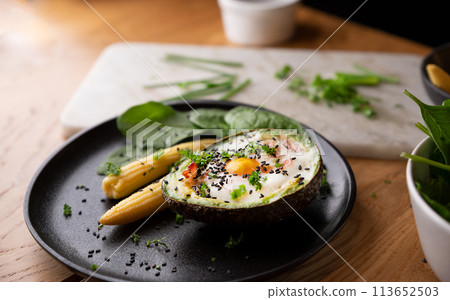 Cooking Avocado with Egg and Bacon. The girl prepares a healthy meal, close-up of her hands and 113652503
