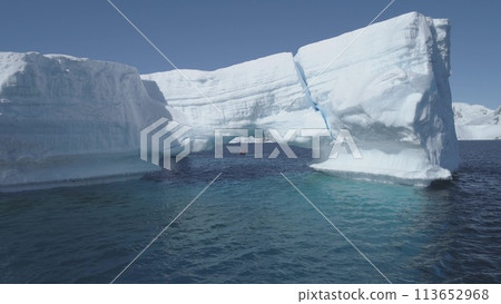 Antarctica iceberg aerial zoom out view drone flight. Overview snow ice mountains archipelago among polar winter ocean. Harsh environment. 113652968