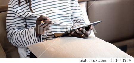 Smiling young African American man using digital tablet remote job sitting on the bed at home. concept online technology communication 113653509