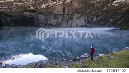 Sporty girl looking into reflection of mountains in lake. Lake Oeschinensee in Swiss alps. Travel, adventure, healthy lifestyle, wanderlust concept. Sporty girl looking into reflection of mountains in lake. Lake Oeschinensee in Swiss alps. Travel, adventure, healthy lifestyle, wanderlust concept. 113654402