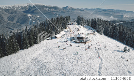 Winter active sport resort at snow mountain top aerial. People at nature landscape. Ski slope at fir forest. Mount ranges with pine trees. Tourist attraction at Carpathians, Bukovel, Ukraine, Europe Winter active sport resort at snow mountain top aerial. People at nature landscape. Ski slope at fir forest. Mount ranges with pine trees. Tourist attraction at Carpathians, Bukovel, Ukraine, Europe 113654698