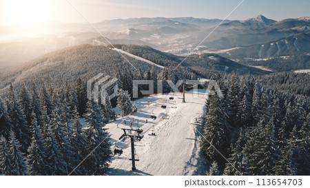 Escalator at sun snow mountain aerial. Winter nature landscape. Tourist attraction at snowy tree. Ski slope at fir forest. Extreme sport. Vacation at Carpathian mounts, Bukovel Resort, Ukraine, Europe Escalator at sun snow mountain aerial. Winter nature landscape. Tourist attraction at snowy tree. Ski slope at fir forest. Extreme sport. Vacation at Carpathian mounts, Bukovel Resort, Ukraine, Europe 113654703