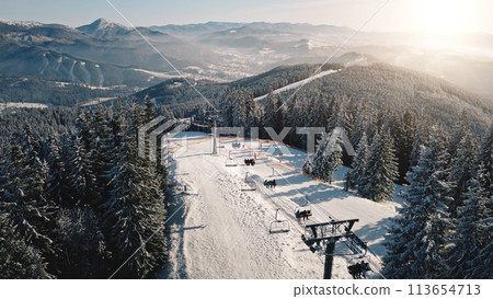 Sun ski resort at snow mountain forest aerial. Escalator chair at pine trees. Tourist attraction. Active sport. Winter vacation at Carpathians mounts, Bukovel, Ukraine, Europe. Travel, tourism scenery 113654713