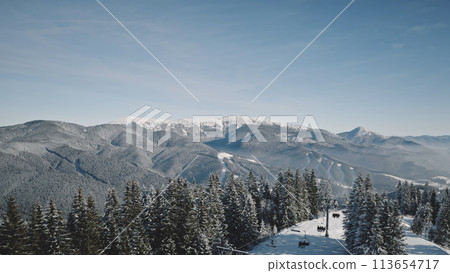People at snow resort cottage aerial. Active sport at sun mountain. Snowy ski slope at tourists attraction. Winter nature landscape. Fir forest at Carpathian mounts, Bukovel, Ukraine, Europe 113654717