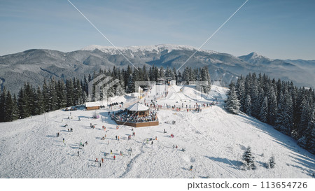 Active winter sport at mountain aerial. Snow ski slope at tourists landmark. People at resort cottage. Snowy nature landscape. Fir pine trees forest at Carpathian mounts, Bukovel, Ukraine, Europe Active winter sport at mountain aerial. Snow ski slope at tourists landmark. People at resort cottage. Snowy nature landscape. Fir pine trees forest at Carpathian mounts, Bukovel, Ukraine, Europe 113654726