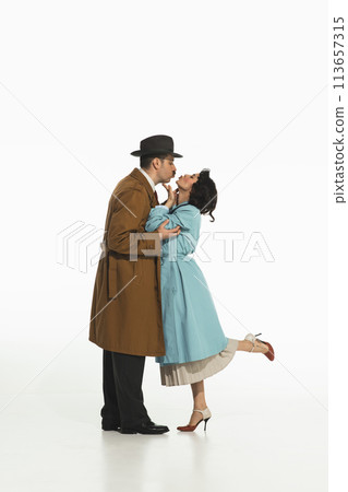 Portrait of happy young couple, man and woman in retro-styled clothes, coats standing and kissing. 113657315
