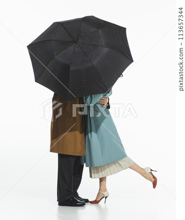 Elegant couple, man and woman in trench coat standing and kissing under umbrella isolated on white background. Elegant couple, man and woman in trench coat standing and kissing under umbrella isolated on white background. 113657344