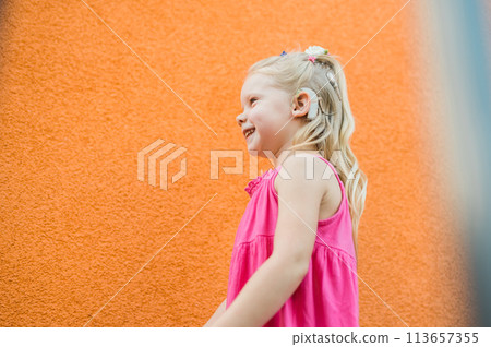 Child girl walks and have fun outdoor with cochlear implant on the head. Hearing aid and treatment concept. Copy space vertical. Inclusion Child girl walks and have fun outdoor with cochlear implant on the head. Hearing aid and treatment concept. Copy space vertical. Inclusion 113657355